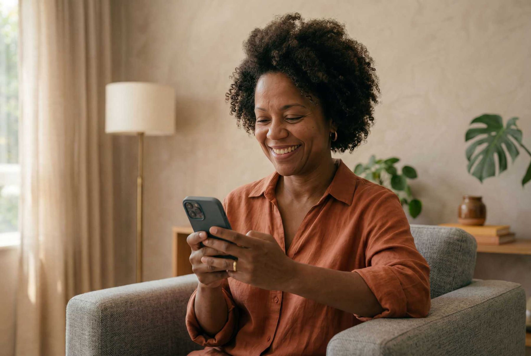 Colaboradora sorrindo no sofá usando o celular